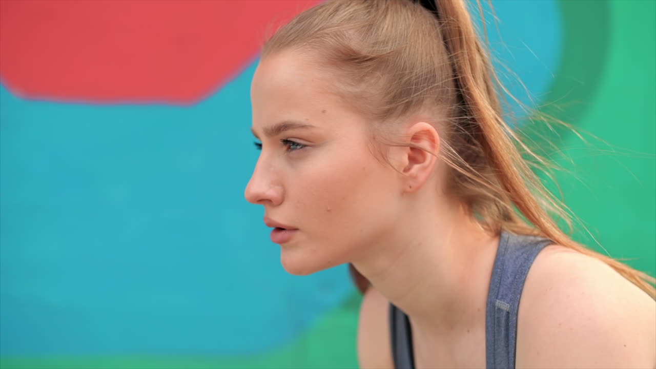 Young focused blonde woman at outdoors training preparing to starting running, multicolored background. Slow motion