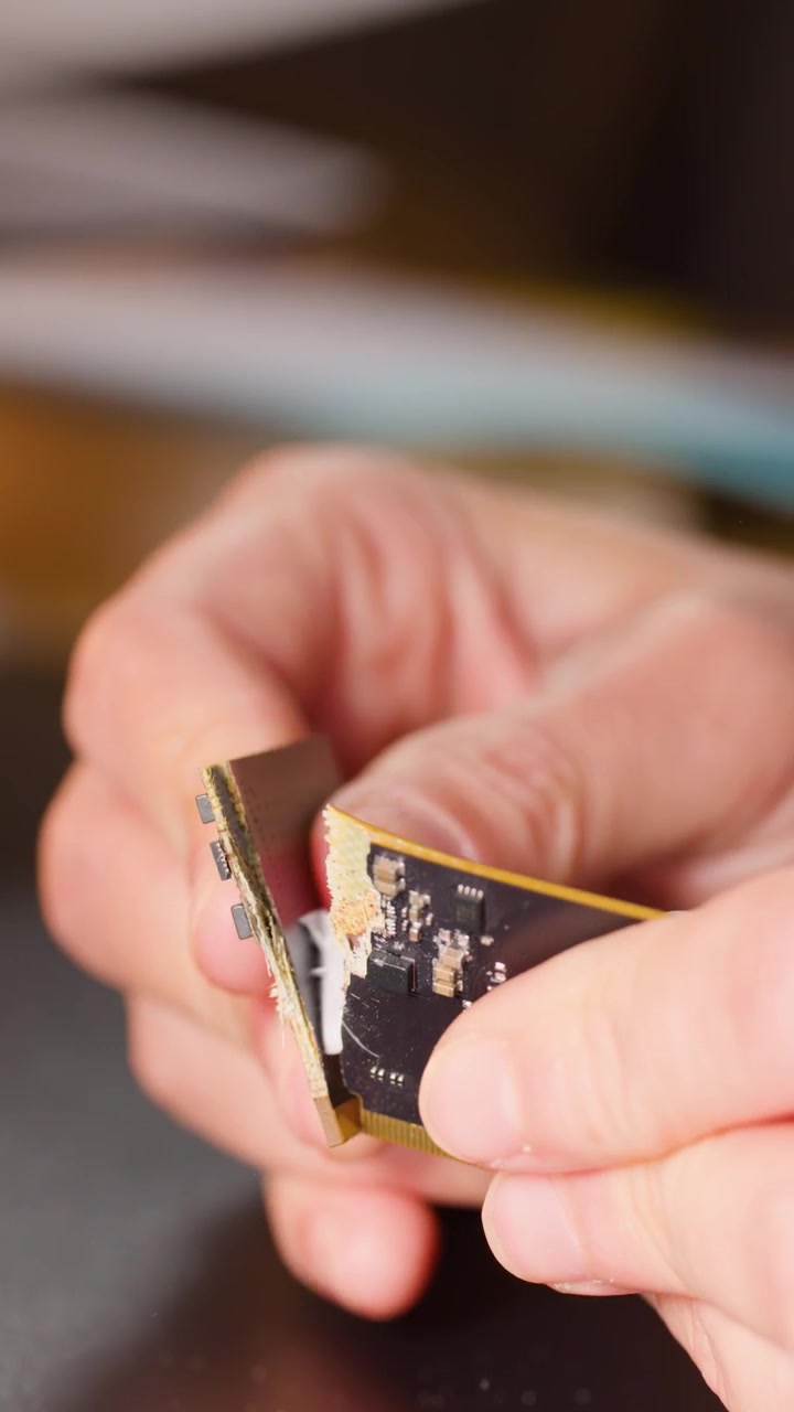 Close-up shot of hands snapping a computer circuit board, showing internal components and hardware destruction