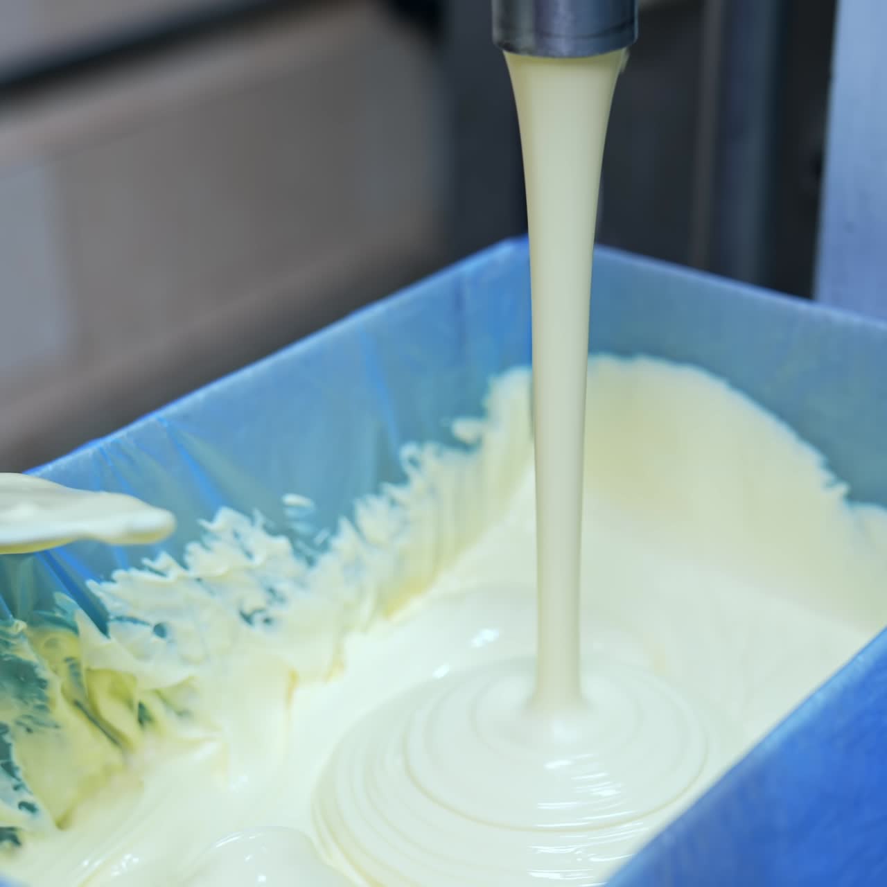 Factory for butter production. Creamy white dairy product pouring into box. Making fresh butter on a milk farm. Dairy product manufacturer. Hand of worker is mixing butter. Close-up