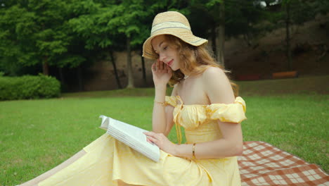 beautiful young woman in strapless dress sitting on picnic blanket reading book