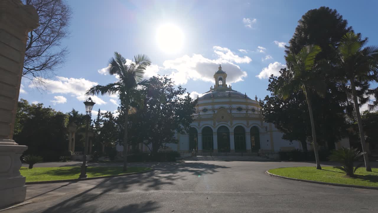 Sunlight illuminates the historic Casino de la Exposition in Seville, Spain, surrounded by palm trees and clear blue skies, showcasing its architectural beauty