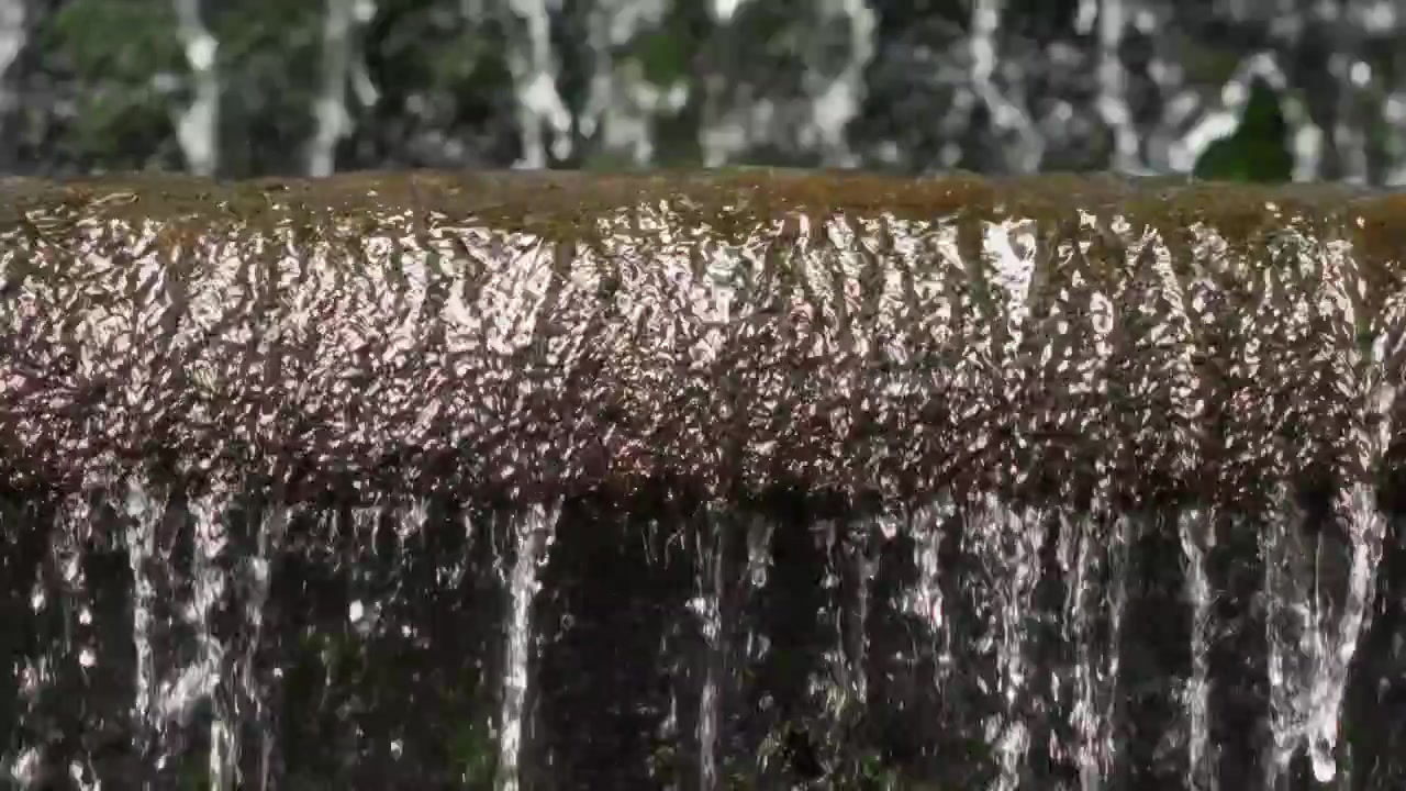 Clear running water ripples heavily across an artificial stone barrier before falling.