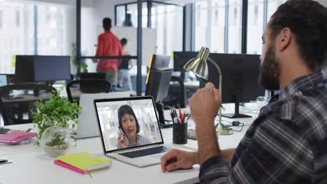 Mixed-race-businessman-sitting-at-desk-using-laptop-having-video-call-with-female-colleague