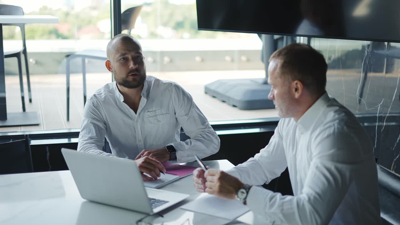 Two diverse business men discussing financial market data using laptop and digital tablet. Financial advisor broker manager consulting investor client about digital investment at office meeting