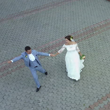 charming stylish newlyweds are holding hands while walking along the sunny town street. aerial view. square video