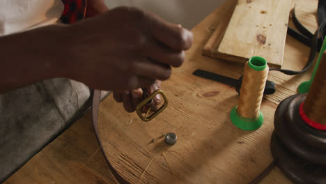 manos de un artesano afroamericano usando herramientas para hacer un cinturón en un taller de cuero