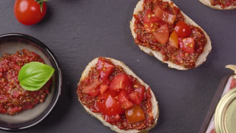 Vista-Panorámica-De-La-Deliciosa-Bruscetta-Con-Productos-Frescos,-Tomates,-Albahaca-Y-Aderezo-Picante-Servidos-En-Una-Fuente-De-Pizarra,-Girando-Con-Un-Aderezo-Al-Costado