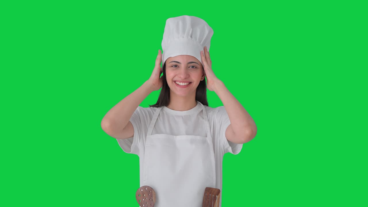 Felice chef professionista indiana con cappello e grembiule, su sfondo verde
