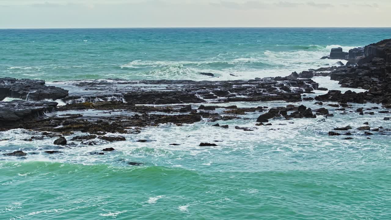 órbita telefotográfica aérea alrededor de las olas del océano en erupción contra pilares de basalto oscuro