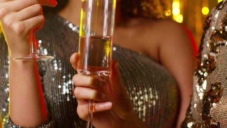 close up of two women in nightclub or bar celebrating drinking alcohol with sparkling lights