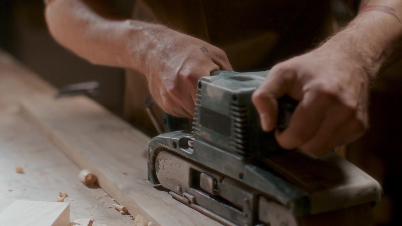 Falegname che rifinisce un'asse di legno con levigatrice a nastro elettrica