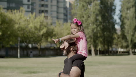 Little-girl-sitting-on-fathers-neck-and-showing-way-with-hand