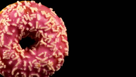 donut de vidrio rosado con salpicaduras sobre un fondo negro.