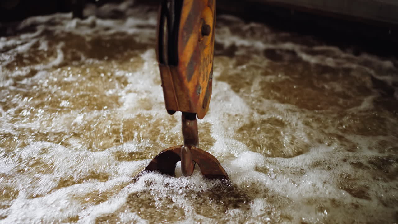 Crane hook submerging into foamy water in a dynamic industrial metal quenching process