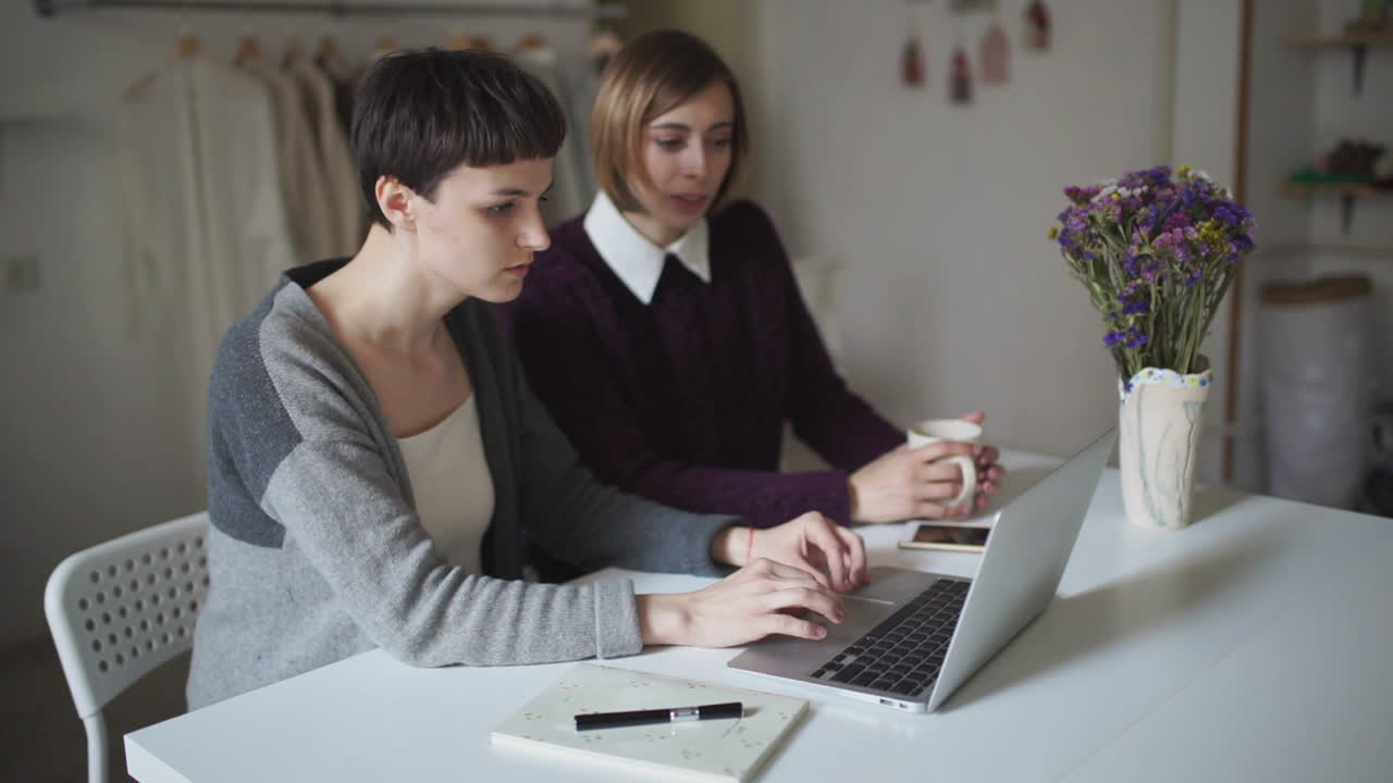 Two young woman spend leisure and using laptop sitting at table in home