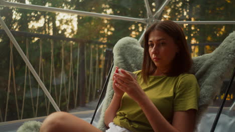 pensive woman picks fingers on cup of coffee sitting in armchair. young woman thinks deeply without changing facial features in comfortable glamping balcony