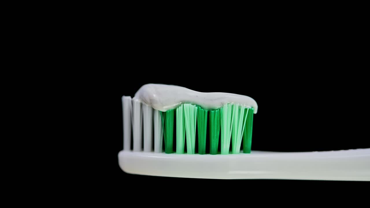 un zoom de un cepillo de dientes con cerdas blancas y verdes cargadas con pasta de dientes que revela un fondo oscuro