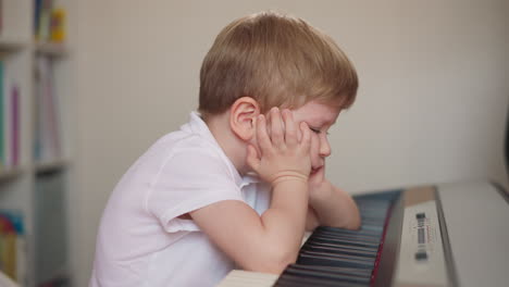 el niño deja de tocar el piano y pone los codos en el teclado