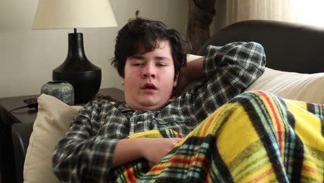 tired sick teenage boy lying on sofa at home and sneezing