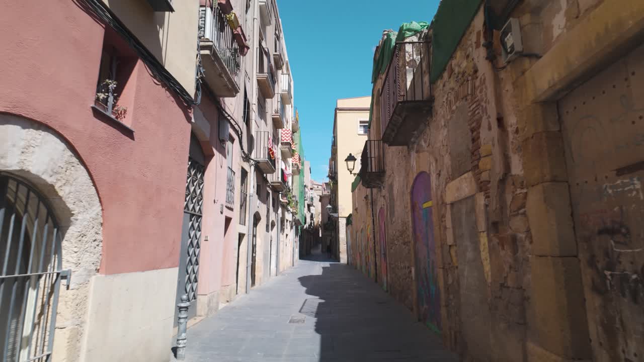 POV walking along Cobblestone street cutting through historic buildings in Tarragona, Spain, bathed in sunlight