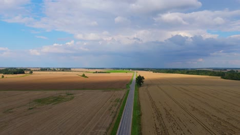 drone flight over golden wheat fields and country road on a sunny summer day with rainbow in the sky peaceful latvian countryside aerial view