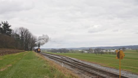 an approaching steam passenger train blowing smoke and steam on a cloudy day