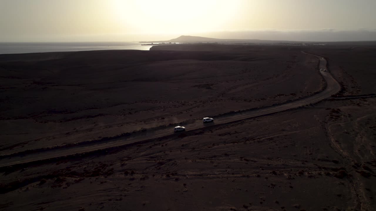 vista aérea de los autos que conducen el camino polvoriento en el desierto durante la puesta del sol