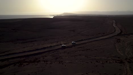 aerial view of cars driving the dusty road on the desert during late sunset