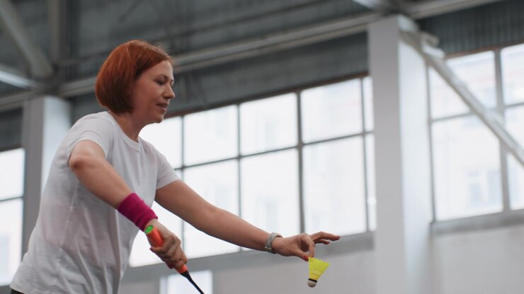 Indoor badminton practice white player executing powerful smashes and precise drives, intense footwork, concentrated expression, wristband accent, bright gym windows, focused training