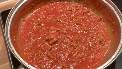 bolognese sauce with minced meat is cooking in a pan on the stove