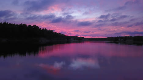 aerial backward drone shot close to the water, above a lake and towards the forest, a purple sky, at a colorful sunset or dusk, at albysjon, tyreso, sweden