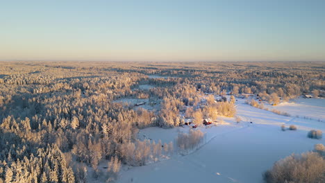 Winter-sunrise-over-a-serene-Nordic-village-with-snow-covered-houses-and-forests,-aerial-view