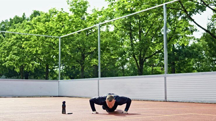 Young handsome man in black shorts doing exercises on the sports ground. Man doing sports outdoors in the city park. Healthy lifestyle