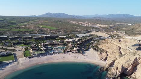 aerial dolly backwards shot of a gorgeous beach with hotel facilities and blue sea with majestic cliffs at santa maria beach in cabo san lucas during a beautiful vacation