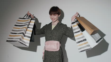 Cheerful-Girl-Walking-in-Studio-and-Posing-with-Shopping-Bags