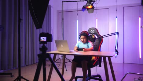 excited asian little boy playing video game with mobile phone while live stream, professional light equipment