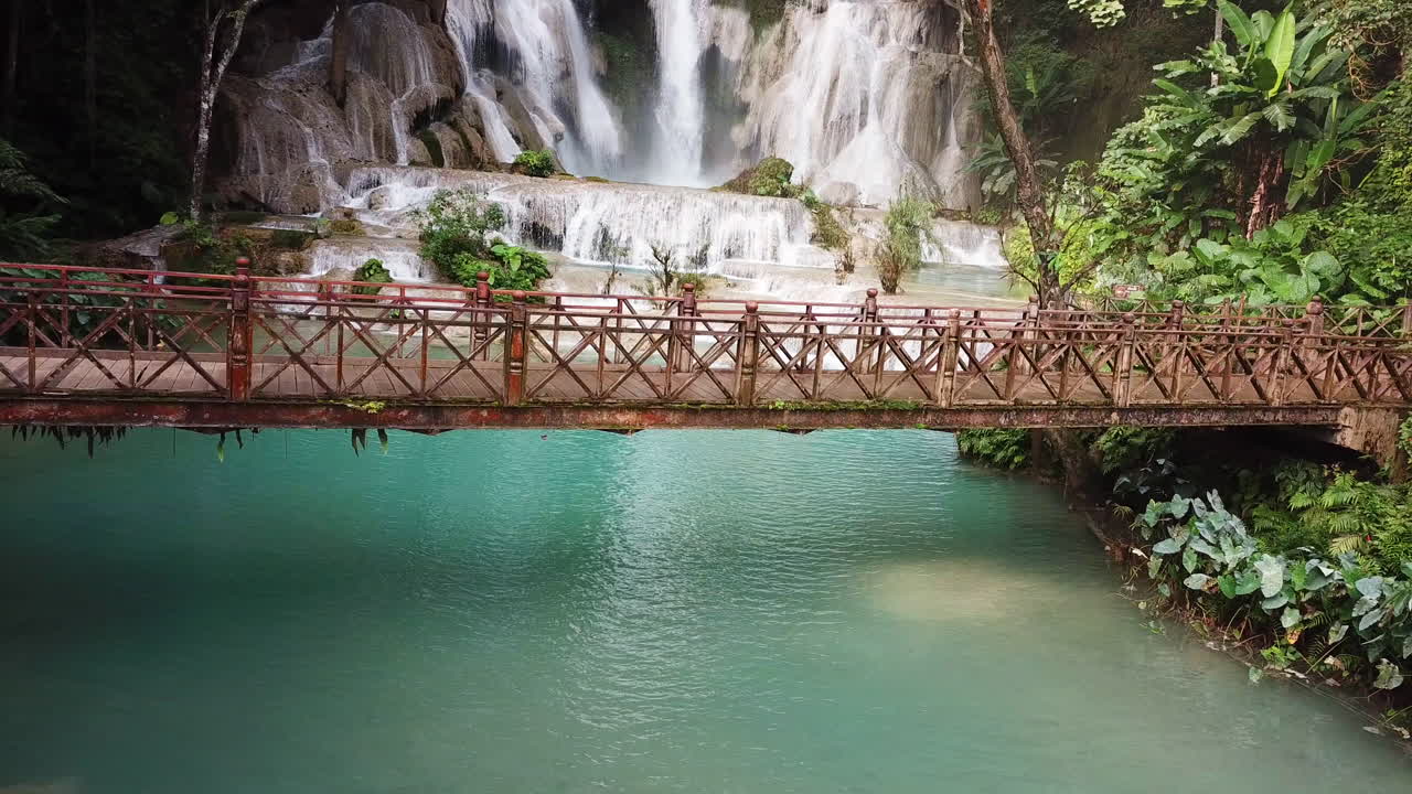 Pemandangan surgawi eksotis, aerial statis, jembatan kayu di bawah air terjun menakjubkan di Laos, Air Terjun Kuang Si.