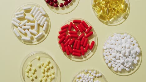 video of a variety of pills and capsules in glass dishes on yellow background