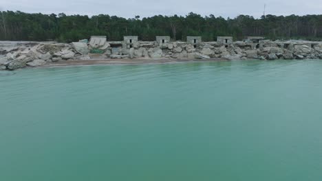 Aerial-view-of-abandoned-seaside-fortification-buildings-at-Karosta-Northern-Forts-on-the-beach-of-Baltic-sea-,-overcast-day,-wide-drone-shot-moving-forward-over-the-sea