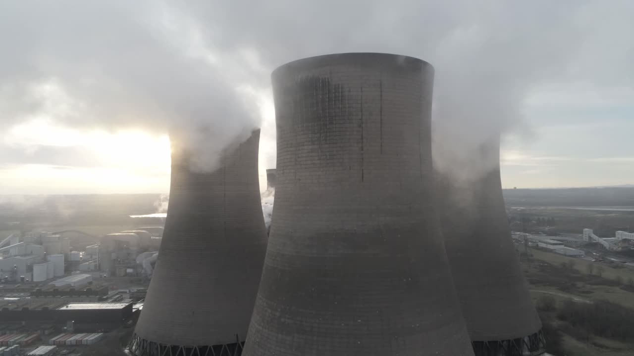 dolly lento aéreo justo al otro lado de las torres de refrigeración de la central eléctrica emisiones de vapor de humo mientras el amanecer se esconde detrás de la torre
