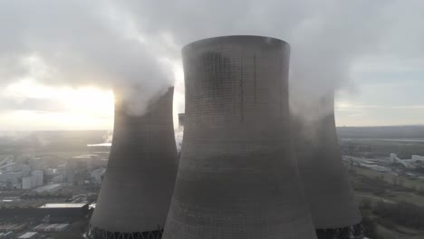 aerial slow dolly right across power station cooling towers smoke steam emissions as sunrise hides behind tower