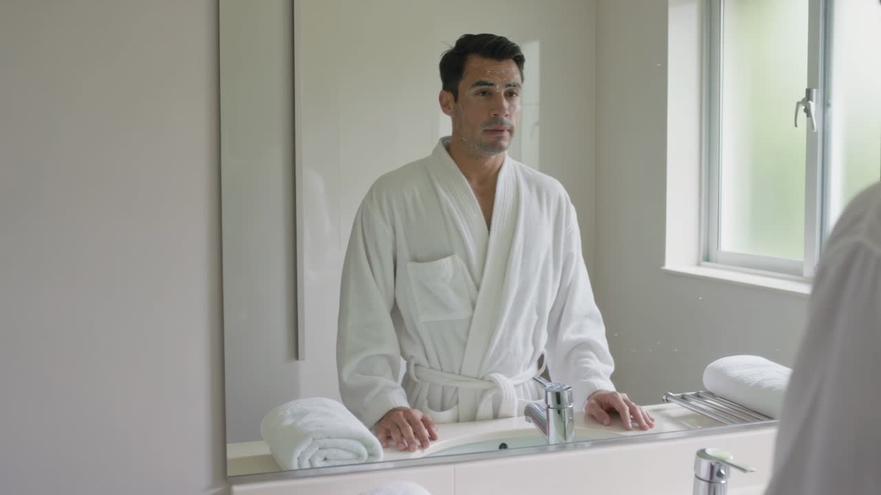 Man in Bathrobe Looking at Reflection in Bathroom Mirror