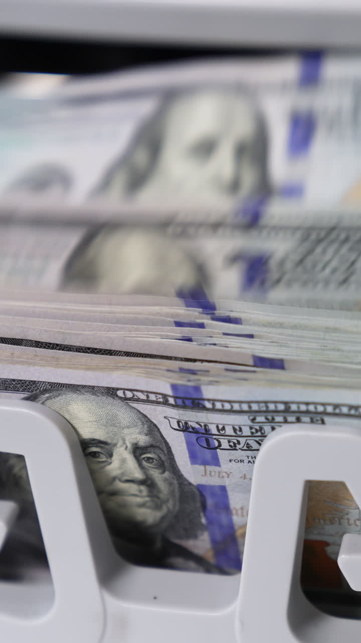 One hundred dollar wad being calculated in money counting machine. Benjamin Franklin portrait on the notes close up. Vertical video