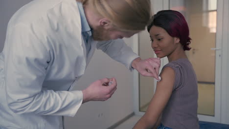 a young doctor with long, blond hair gives an young woman an injection