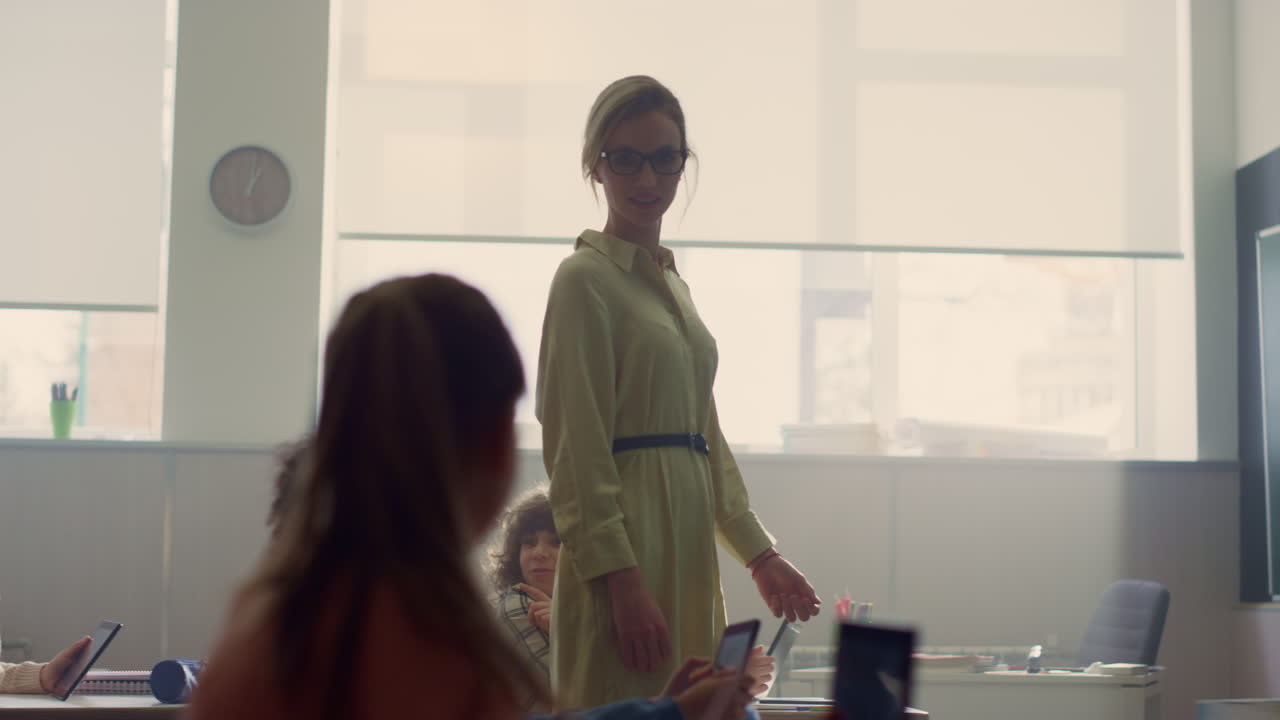 Smart pupils studying with digital tablets. Schoolteacher walking in classroom