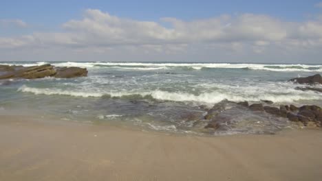 right to left pan of waves crashing into rocks and breaking on shore