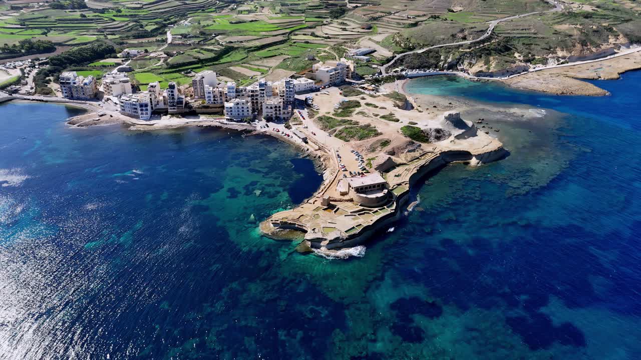 Pemandangan Udara Indah Pulau Gozo, Malta, Menampilkan Garis Pantai Teluk Marsalforn dan Baterai Qolla l-Bajda pada Hari Musim Panas yang Cerah dengan Laut Mediterania Biru Kehijauan dan Lanskap Teras Sawah yang Menghijau