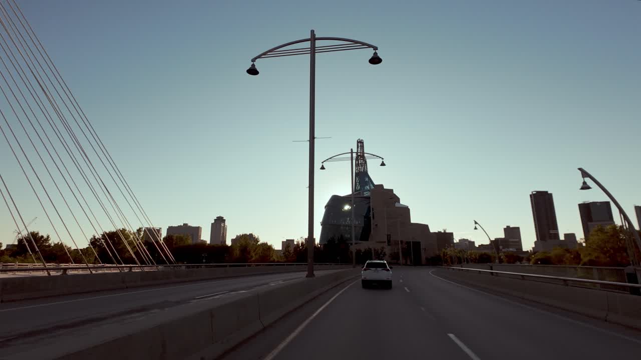 Driving over a bridge in Winnipeg, Manitoba with a view of the Canadian Museum for Human Rights and the city skyline at sunset