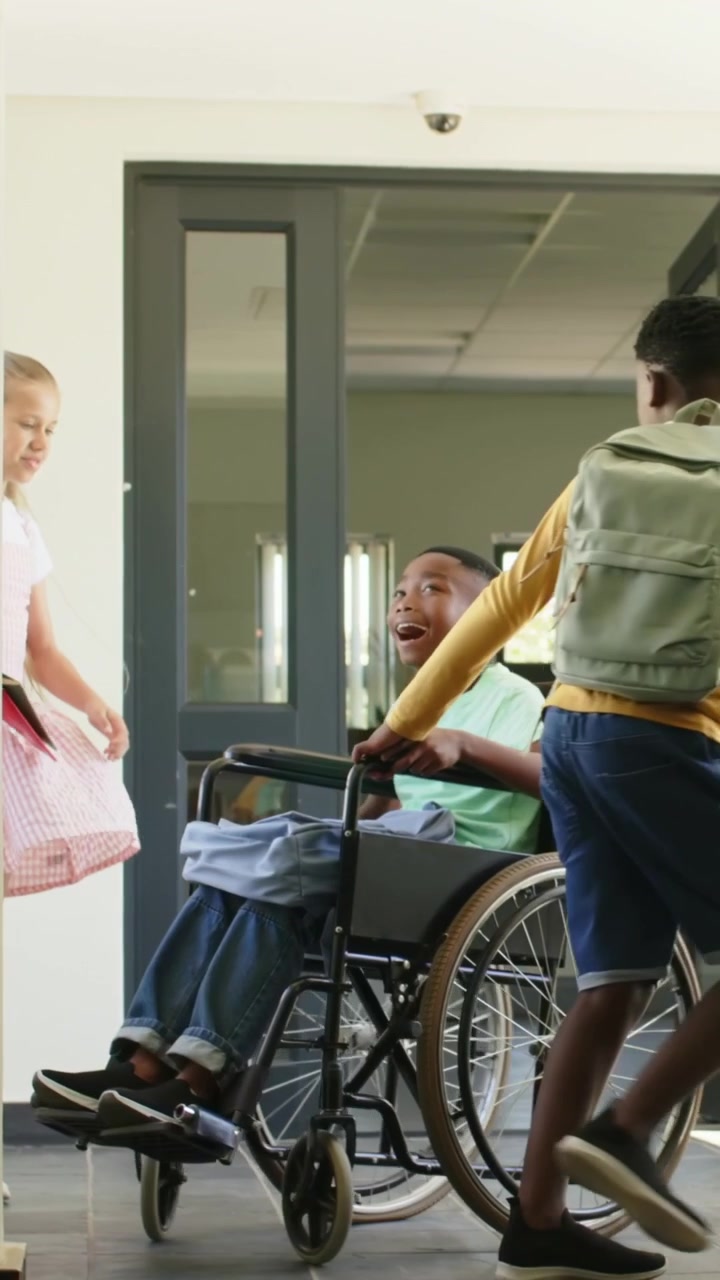 Video verticale: Spingendo un ragazzo in giallo che guida una sedia a rotelle, mentre le porte si aprono all'ingresso della scuola per la classe.