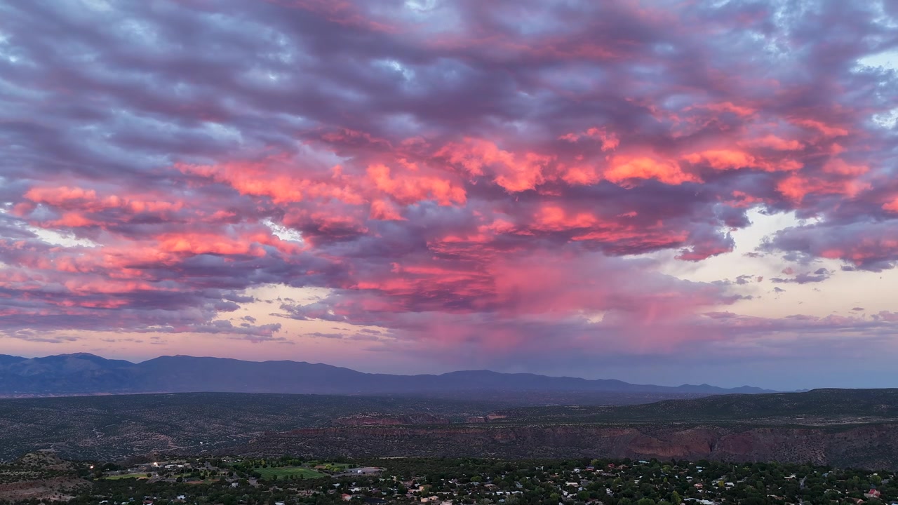 Timelapse 4K con drone di un clima dinamico del sud-ovest e nuvole temporalesche increspate durante il tramonto. Un vasto sistema meteorologico si muove rapidamente sopra, emettendo un bagliore colorato sul paesaggio dell'alto deserto.